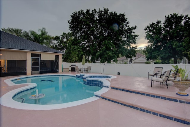 pool at dusk with an in ground hot tub and a patio area