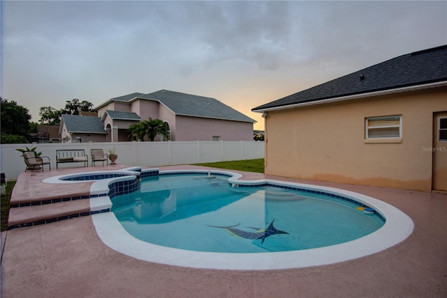 pool at dusk with a patio and an in ground hot tub