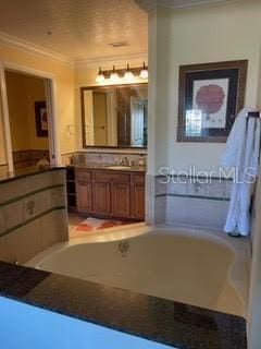 bathroom with a relaxing tiled tub, crown molding, and vanity