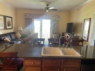 kitchen featuring brown cabinets, dark countertops, a ceiling fan, open floor plan, and a sink