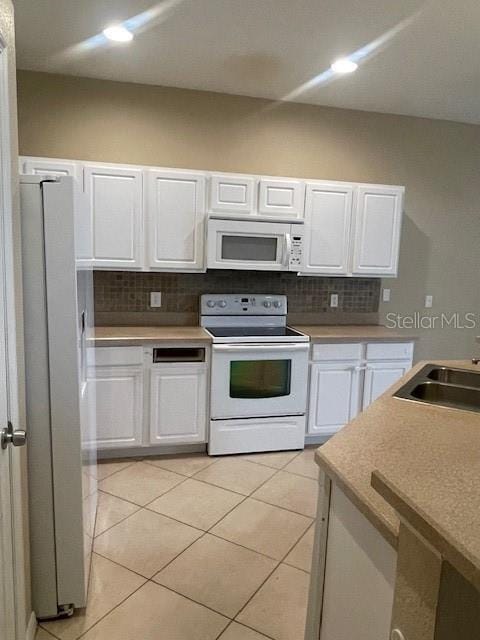 kitchen featuring white appliances, backsplash, and white cabinets