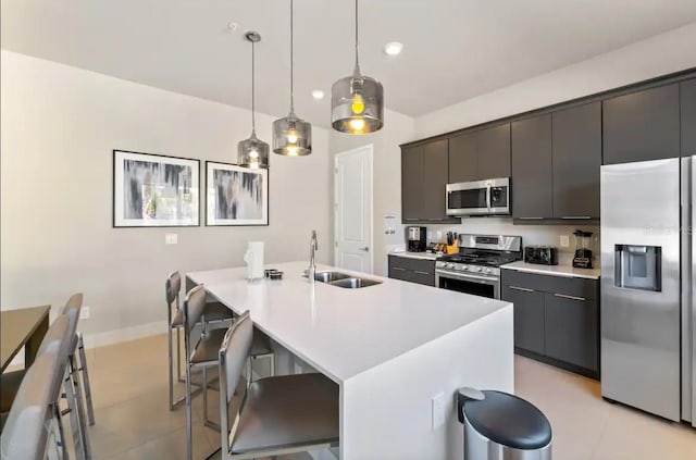 kitchen featuring a kitchen breakfast bar, appliances with stainless steel finishes, sink, decorative light fixtures, and an island with sink