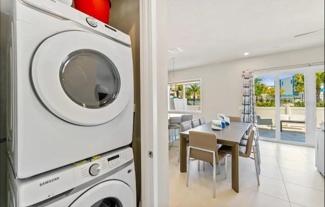 laundry room featuring stacked washer / dryer, light tile patterned floors, and a wealth of natural light