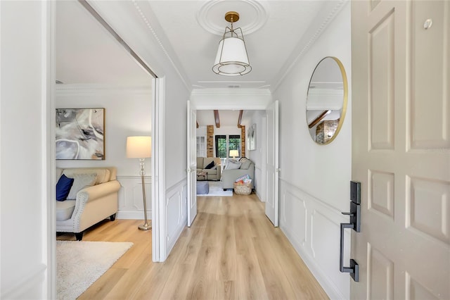 corridor with ornamental molding, beamed ceiling, and light hardwood / wood-style flooring