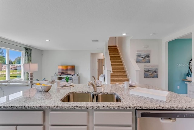 kitchen with light stone counters, sink, white cabinetry, and stainless steel dishwasher