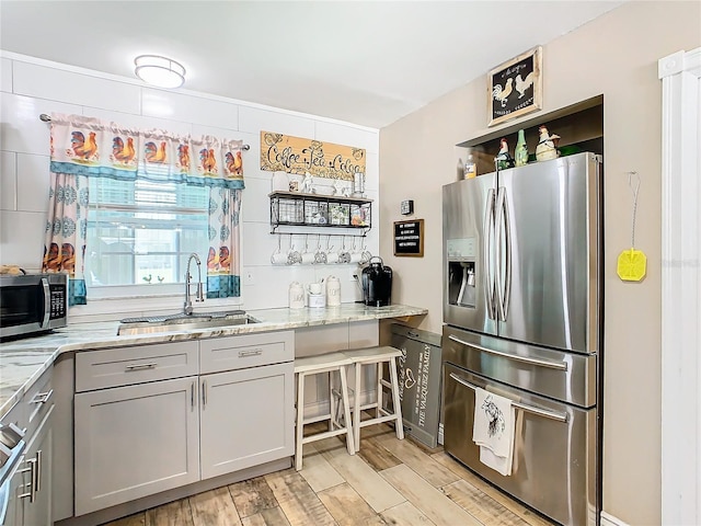 kitchen featuring stainless steel appliances, light stone counters, gray cabinetry, and sink