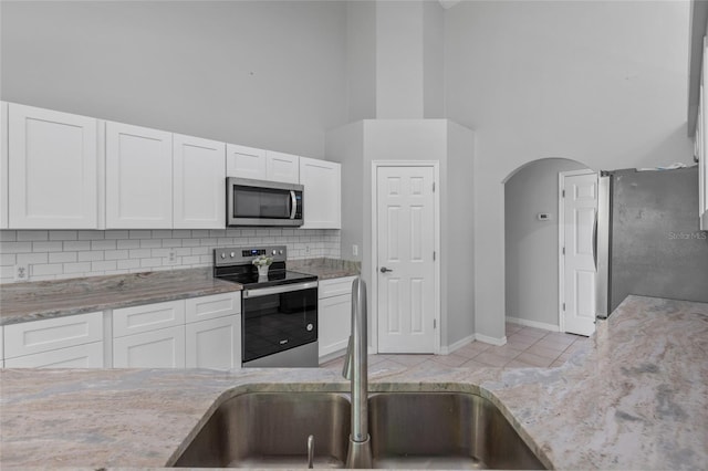 kitchen with light tile patterned flooring, stainless steel appliances, a towering ceiling, and white cabinets