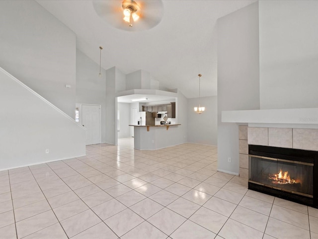 unfurnished living room with a tiled fireplace, light tile patterned floors, ceiling fan with notable chandelier, and high vaulted ceiling