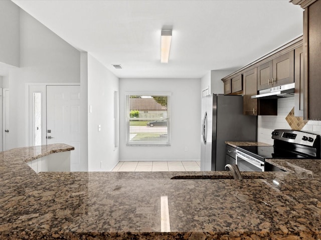 kitchen featuring appliances with stainless steel finishes, backsplash, dark stone counters, light tile patterned floors, and dark brown cabinetry