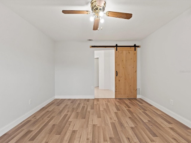 unfurnished room with ceiling fan, a barn door, and light hardwood / wood-style floors