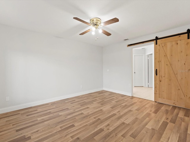 empty room with light hardwood / wood-style floors, a barn door, and ceiling fan