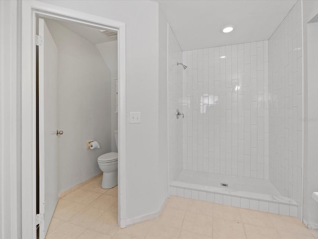 bathroom with tile patterned flooring, a tile shower, and toilet