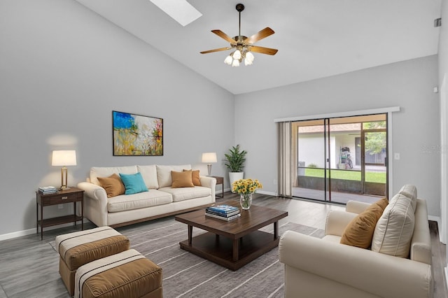 living room with ceiling fan, wood-type flooring, a skylight, and high vaulted ceiling