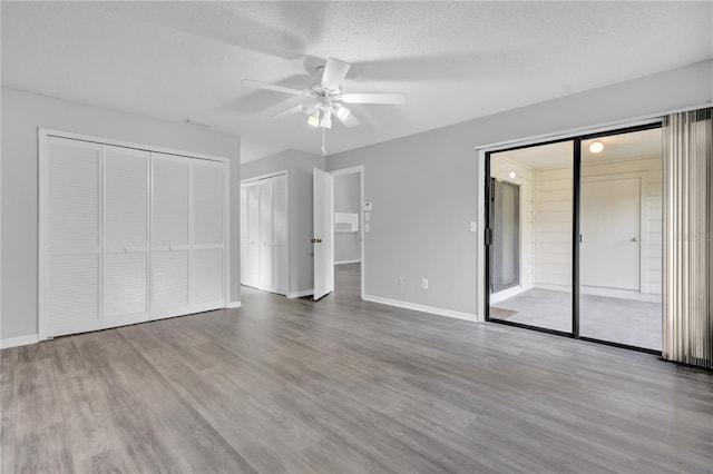 unfurnished bedroom featuring hardwood / wood-style flooring, a textured ceiling, ceiling fan, and two closets