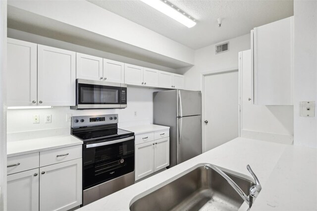 kitchen with appliances with stainless steel finishes, sink, light stone counters, a textured ceiling, and white cabinetry