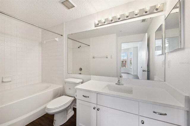 full bathroom with tiled shower / bath, a textured ceiling, toilet, vanity, and hardwood / wood-style floors