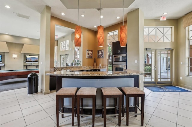 kitchen with visible vents, a kitchen bar, light tile patterned floors, appliances with stainless steel finishes, and a towering ceiling