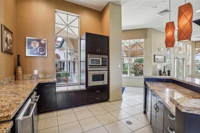 kitchen featuring black microwave, light stone counters, light tile patterned floors, oven, and dark brown cabinetry