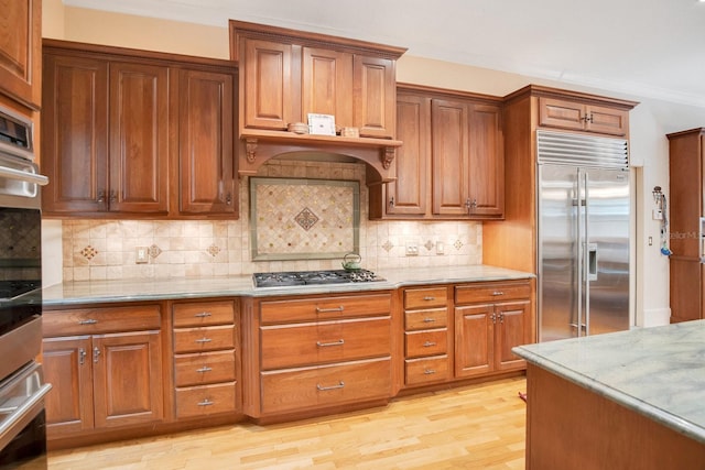 kitchen with tasteful backsplash, appliances with stainless steel finishes, light stone countertops, and light hardwood / wood-style flooring