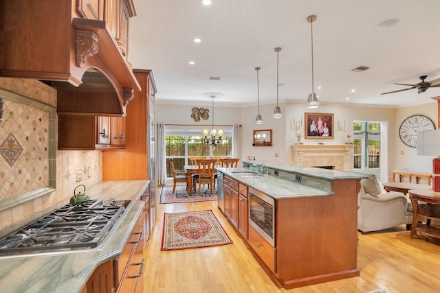 kitchen with decorative light fixtures, stainless steel gas stovetop, custom exhaust hood, a kitchen island with sink, and light wood-type flooring