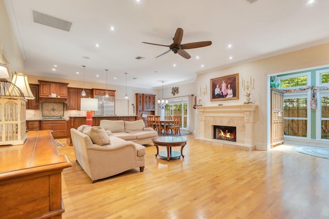 living room with ornamental molding, ceiling fan with notable chandelier, a fireplace, and light wood-type flooring