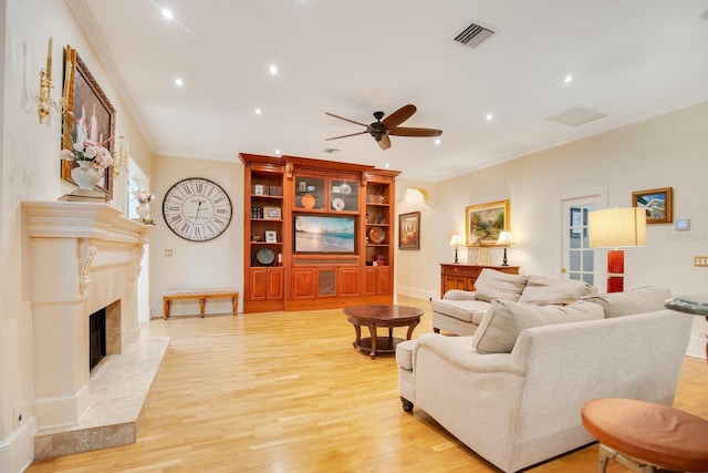 living room with a premium fireplace, ornamental molding, ceiling fan, and light hardwood / wood-style flooring