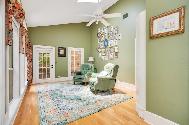 sitting room featuring high vaulted ceiling, hardwood / wood-style floors, ceiling fan, and a skylight