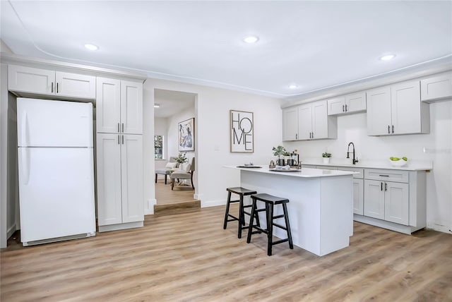 kitchen with white fridge, a breakfast bar, light hardwood / wood-style flooring, a kitchen island, and sink