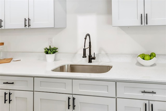 interior details with white cabinets, light stone countertops, and sink