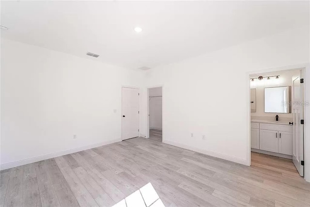 unfurnished bedroom with a closet, light hardwood / wood-style floors, and connected bathroom