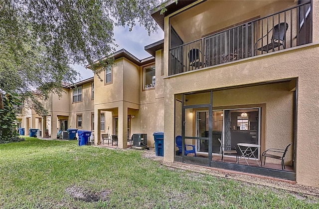 rear view of house with a balcony, a yard, and central AC unit