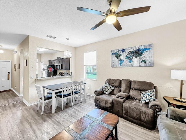 living room featuring a textured ceiling, ceiling fan, and light hardwood / wood-style floors