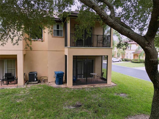 rear view of property with a balcony, central AC, and a lawn