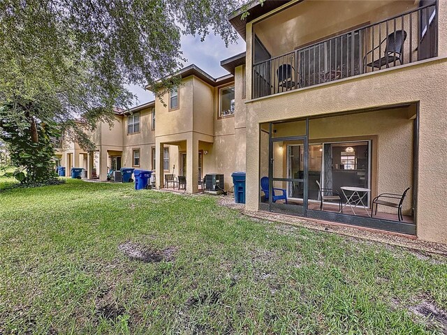 rear view of property featuring a balcony, a yard, and central air condition unit