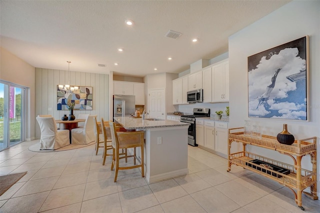 kitchen featuring hanging light fixtures, light stone countertops, an island with sink, stainless steel appliances, and white cabinets