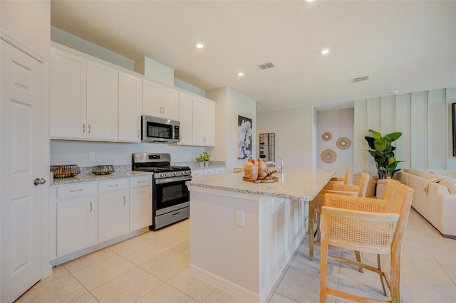 kitchen featuring white cabinetry, stainless steel appliances, light stone counters, light tile patterned floors, and a center island with sink