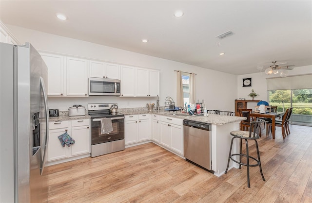 kitchen with stainless steel appliances, white cabinets, light stone counters, light hardwood / wood-style floors, and a kitchen breakfast bar