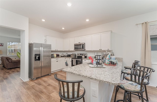 kitchen featuring white cabinetry, light wood-type flooring, light stone countertops, appliances with stainless steel finishes, and kitchen peninsula