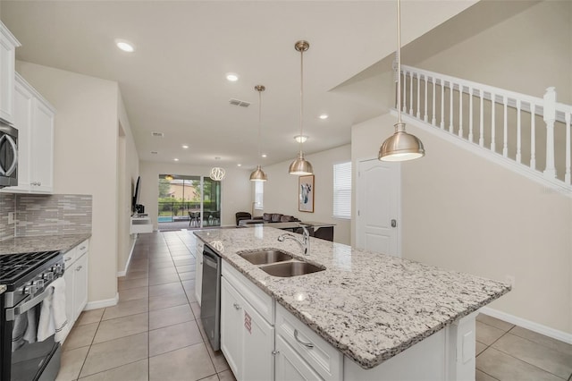 kitchen with stainless steel appliances, decorative backsplash, sink, light stone countertops, and a center island with sink