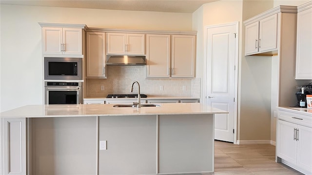 kitchen with a center island with sink, stainless steel appliances, light stone countertops, sink, and backsplash