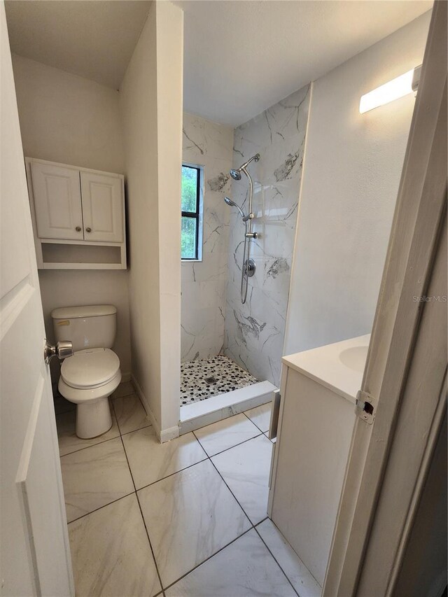 bathroom with tiled shower, tile patterned flooring, toilet, and vanity