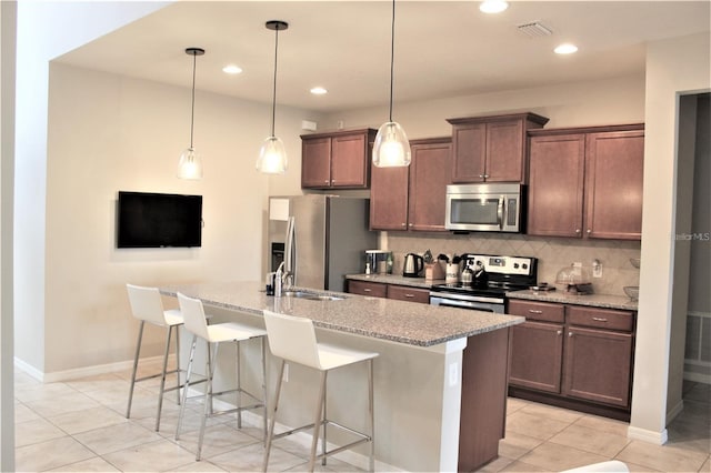 kitchen featuring decorative light fixtures, an island with sink, a breakfast bar area, appliances with stainless steel finishes, and light tile patterned floors