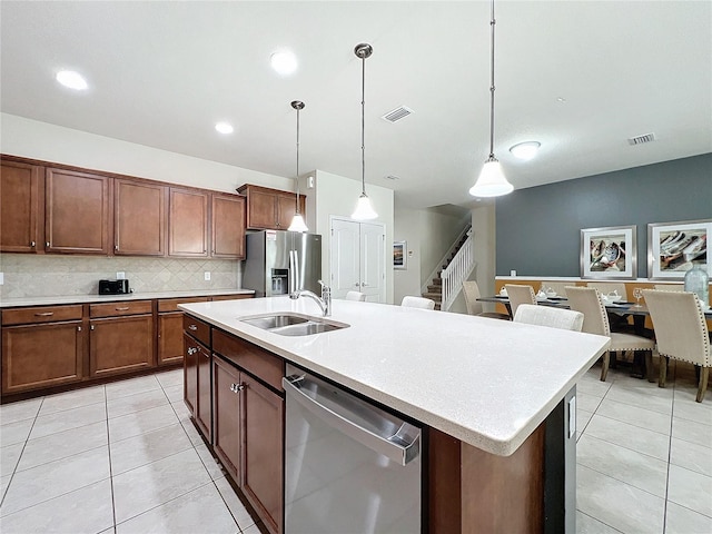 kitchen with sink, hanging light fixtures, appliances with stainless steel finishes, a kitchen island with sink, and decorative backsplash