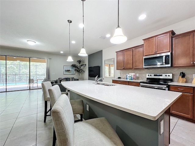 kitchen with sink, decorative light fixtures, stainless steel appliances, and a center island with sink