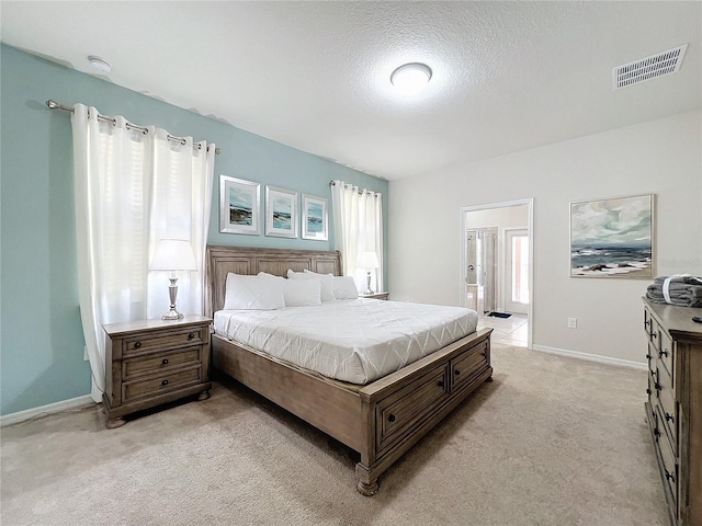 bedroom with multiple windows, ensuite bath, light colored carpet, and a textured ceiling