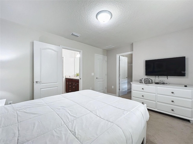 bedroom featuring light carpet, ensuite bath, and a textured ceiling