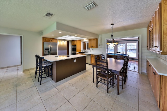 kitchen featuring a center island, backsplash, pendant lighting, a textured ceiling, and appliances with stainless steel finishes