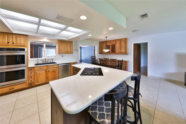 kitchen with a kitchen breakfast bar, stainless steel appliances, sink, light tile patterned floors, and hanging light fixtures