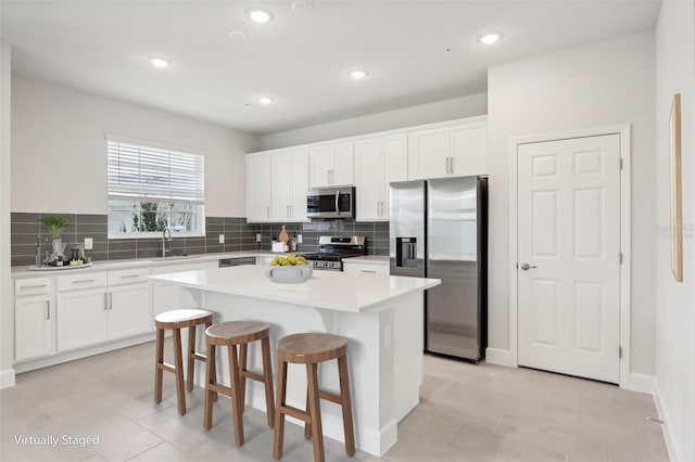 kitchen with a center island, a kitchen breakfast bar, decorative backsplash, white cabinetry, and stainless steel appliances