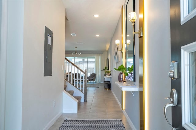 hall with tile patterned flooring, a notable chandelier, and electric panel